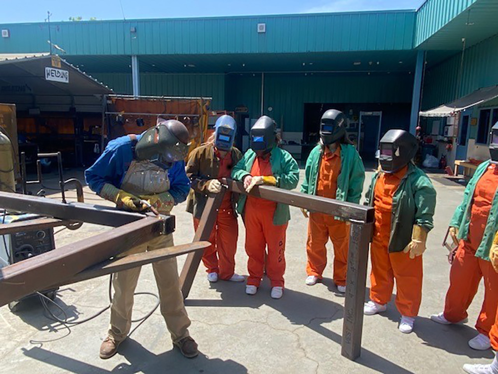 Students in welding masks watch an instructor demonstrate welding techniques at San Jose City College. 