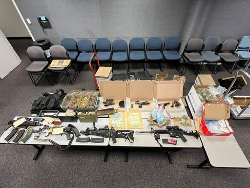 A table full of assault weapons, body armor, ammunition, and drugs that were recovered in a raid of an illegal weapons arsenal.