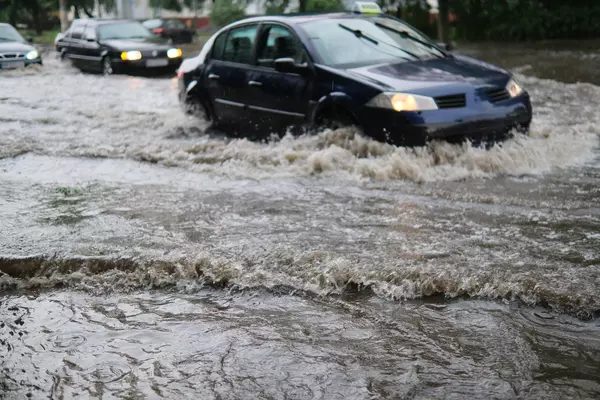 Image of a car driving on a flooded street.