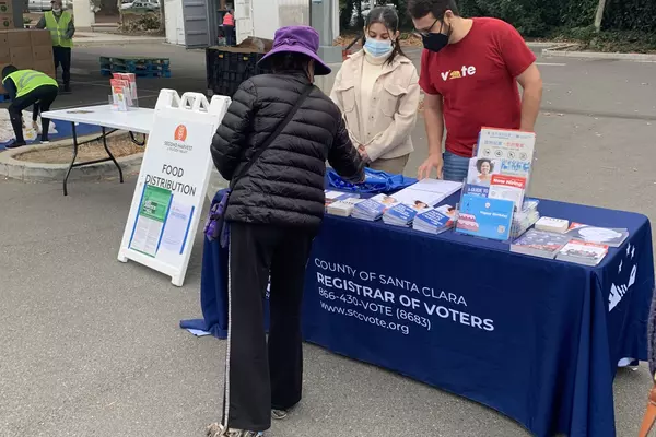 County of Santa Clara Registrar of Voters staff hand out election materials from a table outside at a Second Harvest Food Bank food distribution event. 