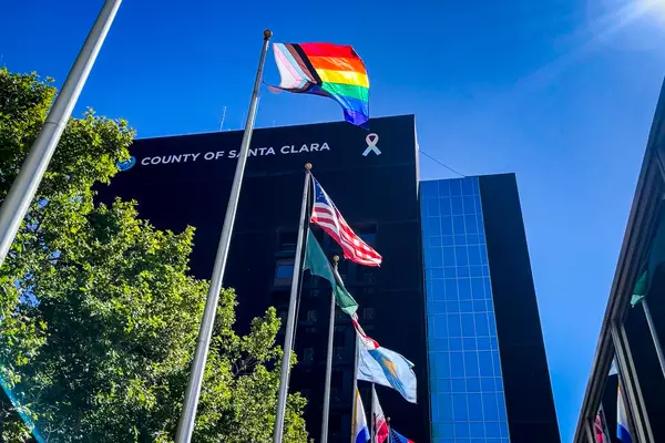 Photo of an LGBTQ-themed rainbow flag being raised in front of County of Santa Clara building on Hedding Street in San Jose.