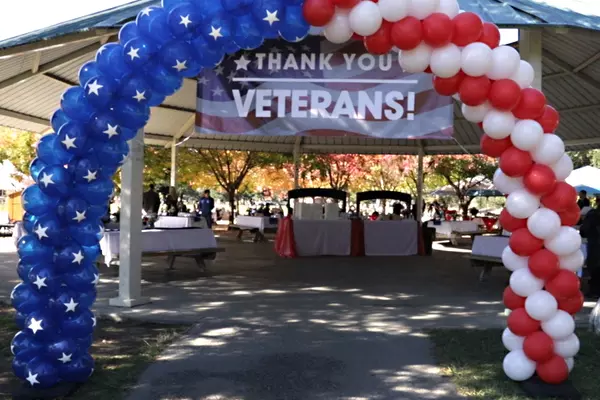 a red, white and blue balloon arch in front of a gazebo. hanging from the gazebo under the arch is a sign that says Thank you Veterans.