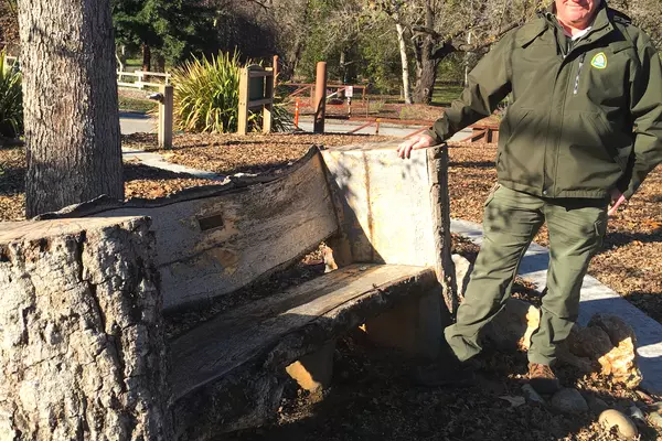 A Parks ranger stands next to a wooden bench.