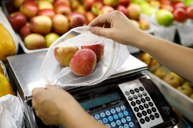 A persons weighs a bag of apple on a digital scale.