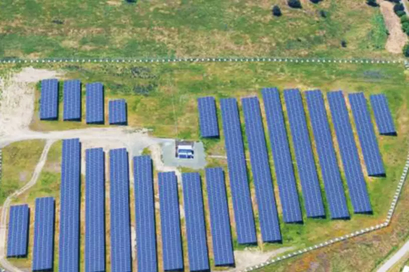 Aerial view of solar panels in a grassy field surrounded by suburban homes.