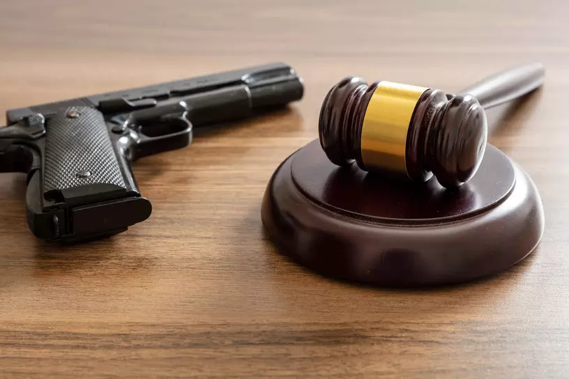 Crime, gun carry and use punishment concept. Judge gavel and handgun on lawyer office desk. Wooden courthouse table, close up view