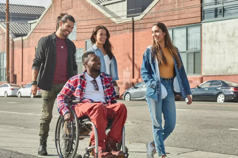 Two women, one man, and one man in a wheelchair going for a stroll outdoors