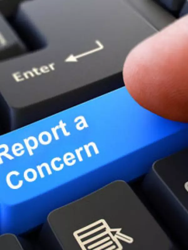 A person clicks on the a key labeled "Report a concern" on a computer keyboard