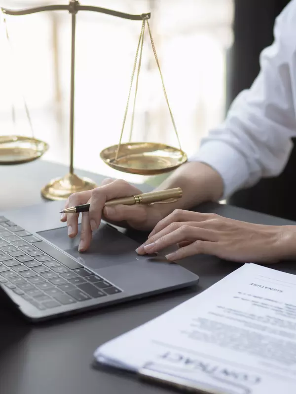 person on a computer with document on side and justice balance in background
