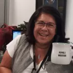 Debbie Ruiz holding a white mug that says, "humble warrior"