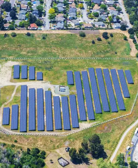 Aerial view of solar panels in a grassy field surrounded by suburban homes.
