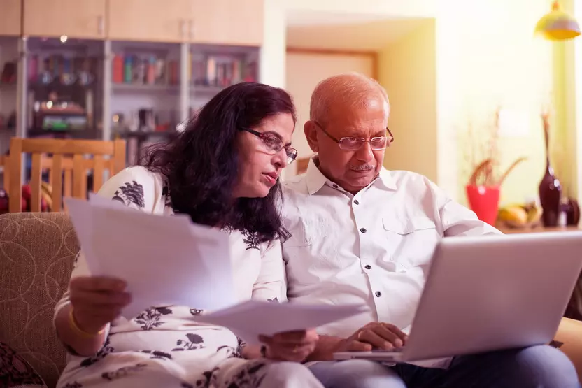 older east Asian Indian male and female on couch looking at paperwork 
