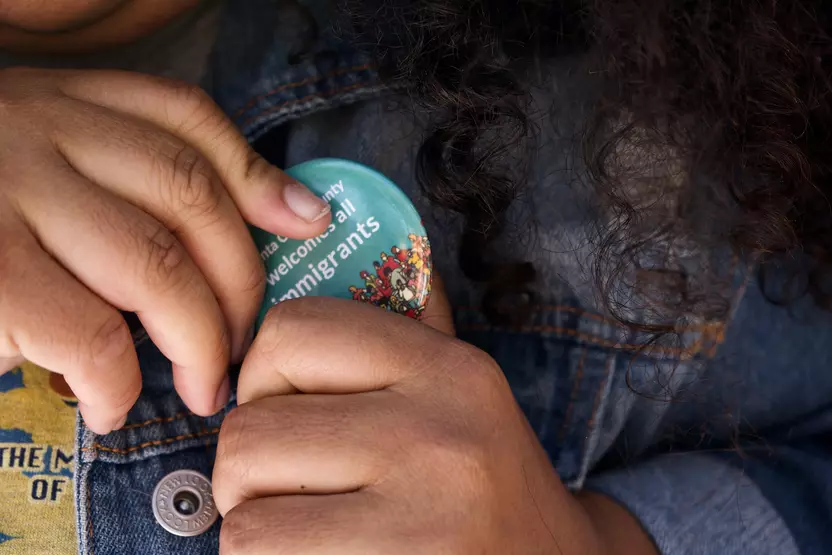 Close up of hands pinning a button that says Santa Clara County welcomes all immigrants to a denim jacket