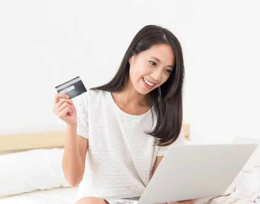 Asian woman holding credit card to make payment on computer